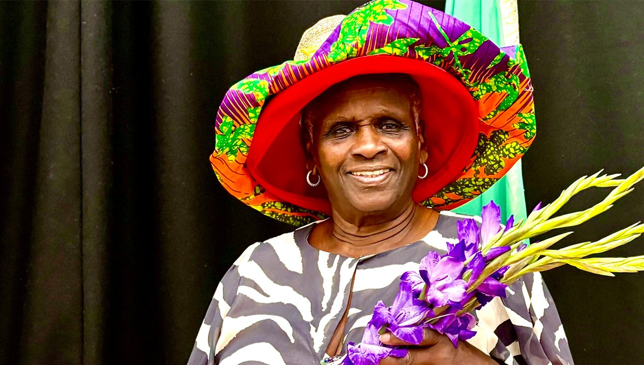 An older black woman in a purple hat holding a digitalis