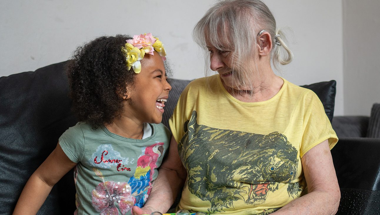 A white grandmother with a hearing aid and a laughing black granddaughter