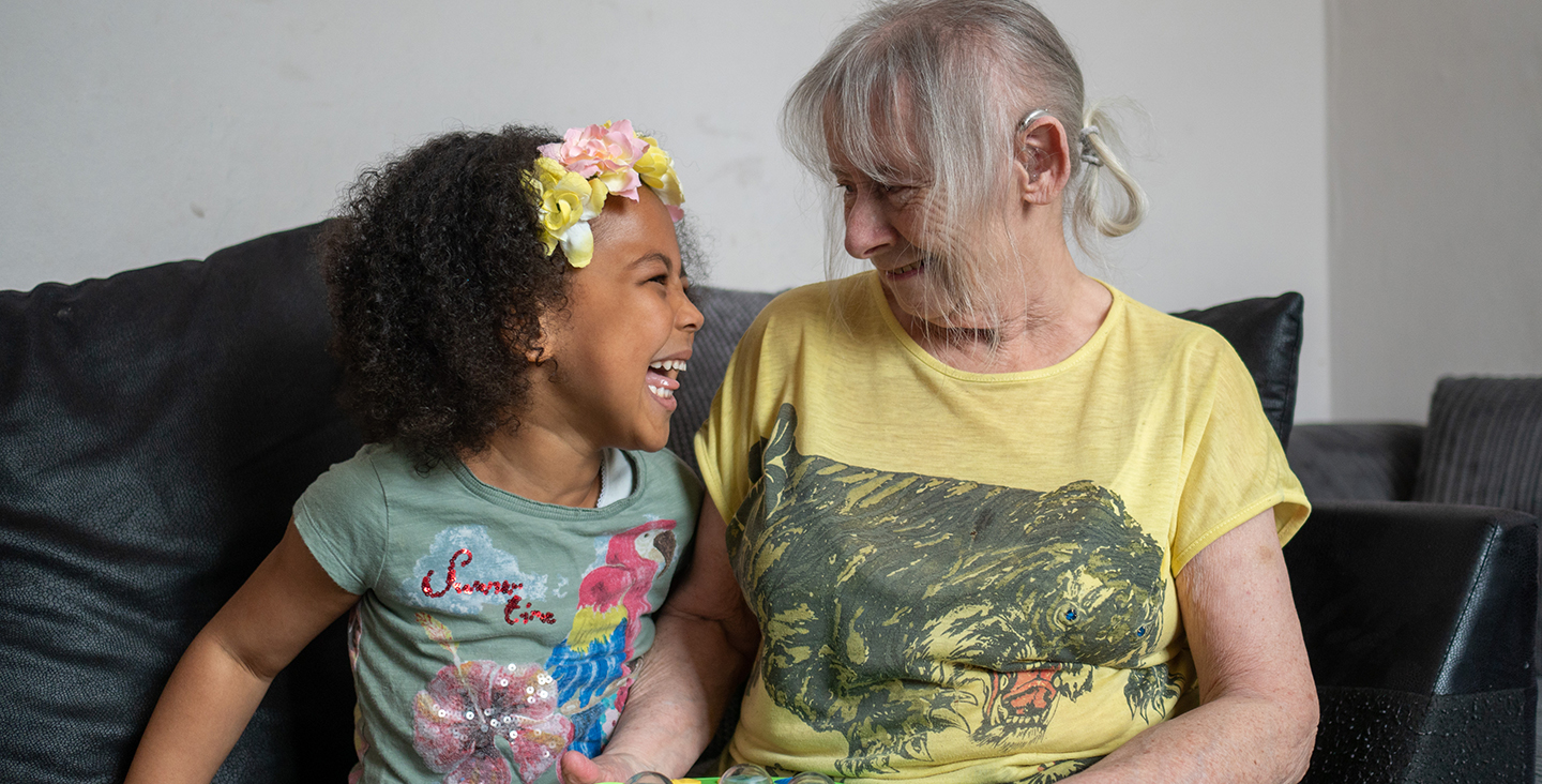 A white grandmother with a hearing aid and a laughing black granddaughter