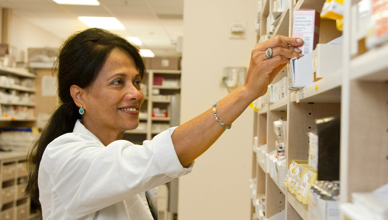 An older Asian female pharmacist taking down a prescription from a shelf