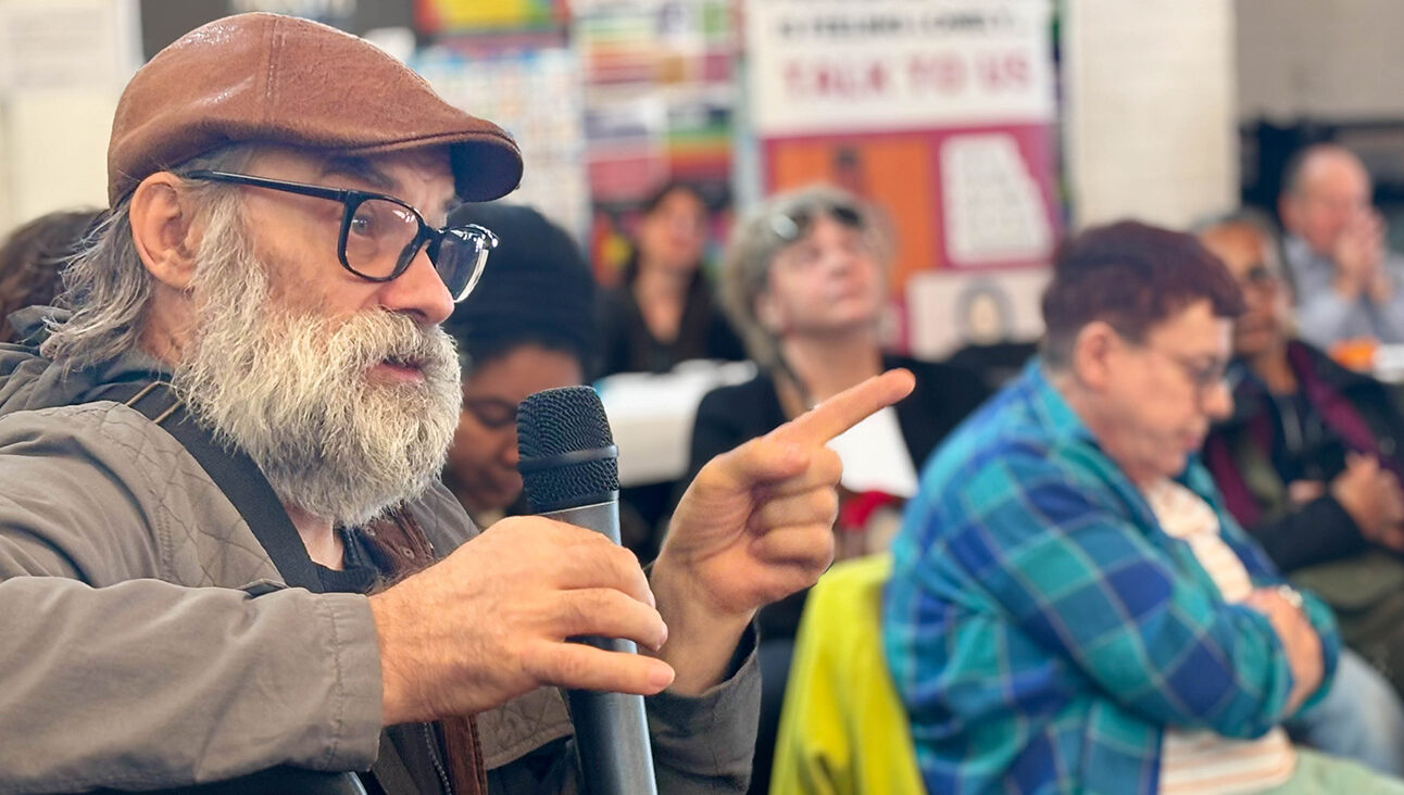 An older white man with a hat and glasses speaking into a microphone at a question and answer event